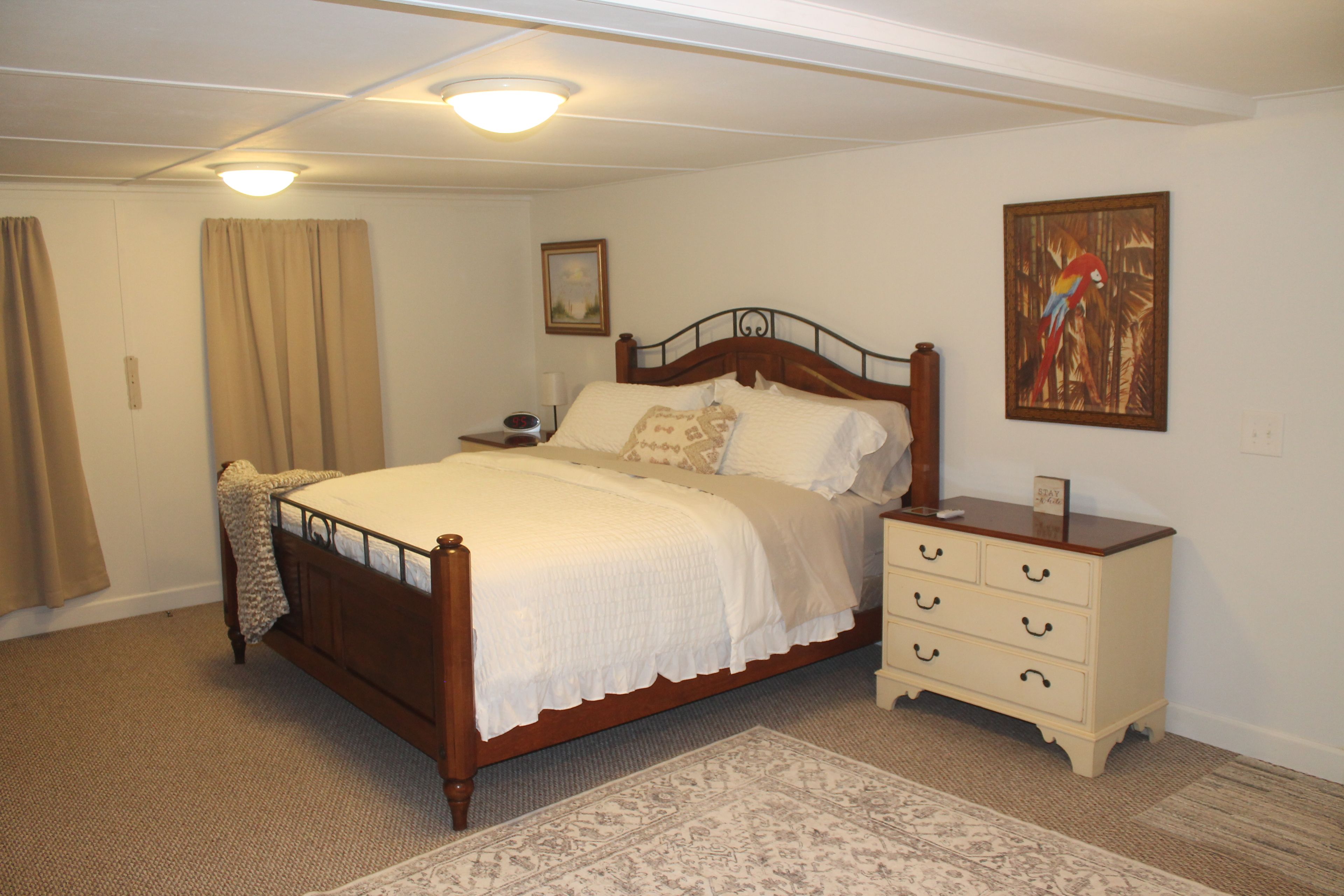 A bedroom with a wooden bed, a nightstand, a dresser, a painting, and a carpeted floor.