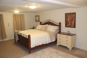 A bedroom with a wooden bed, a nightstand, a dresser, a painting, and a carpeted floor.