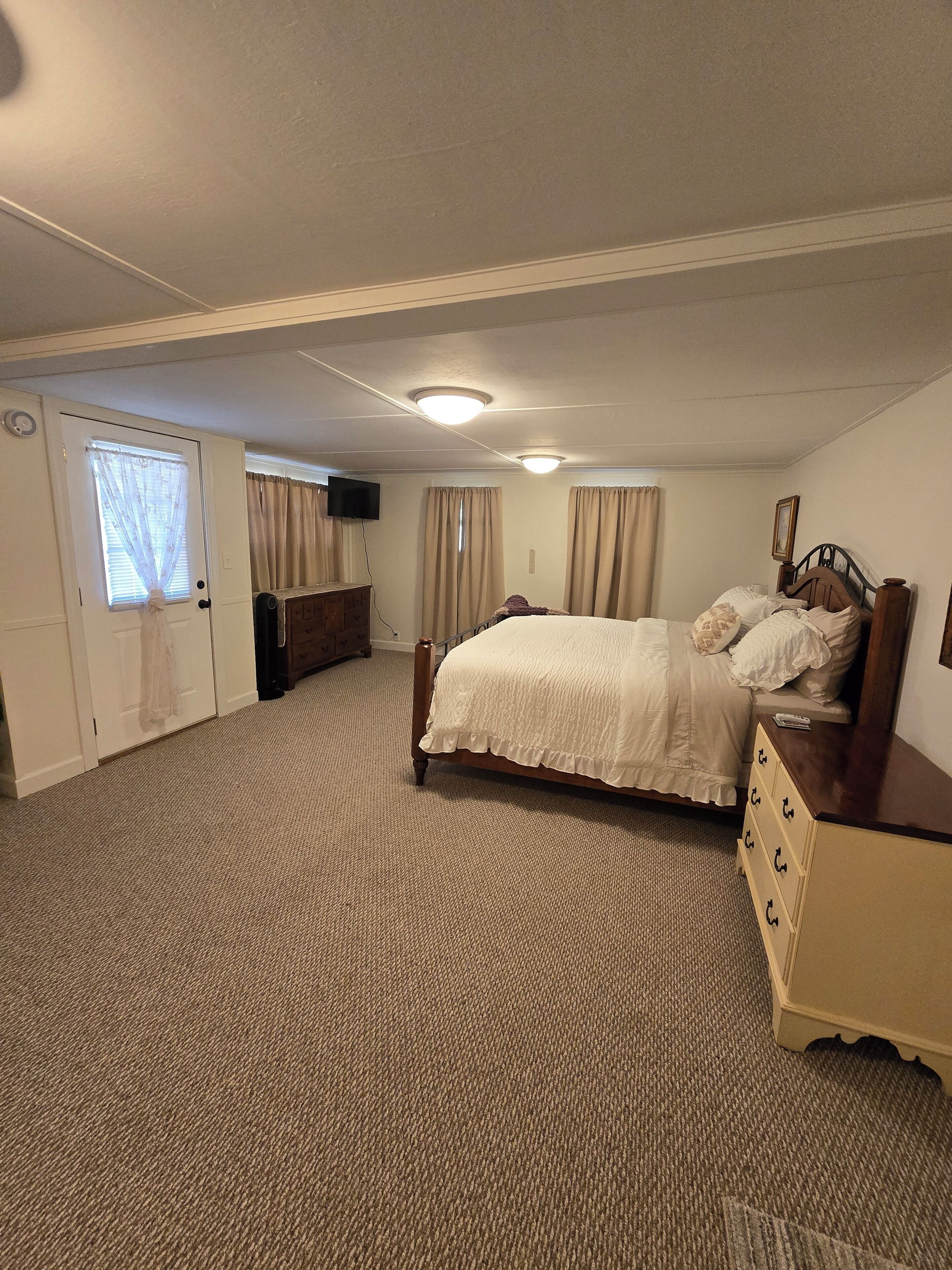 A bedroom with a bed, dresser, and a television on the wall.
