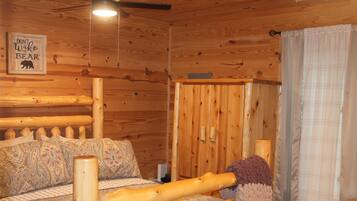 A wooden cabin interior with a bed, a wall-mounted sign, and a window with curtains.