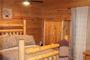 A wooden cabin interior with a bed, a wall-mounted sign, and a window with curtains.