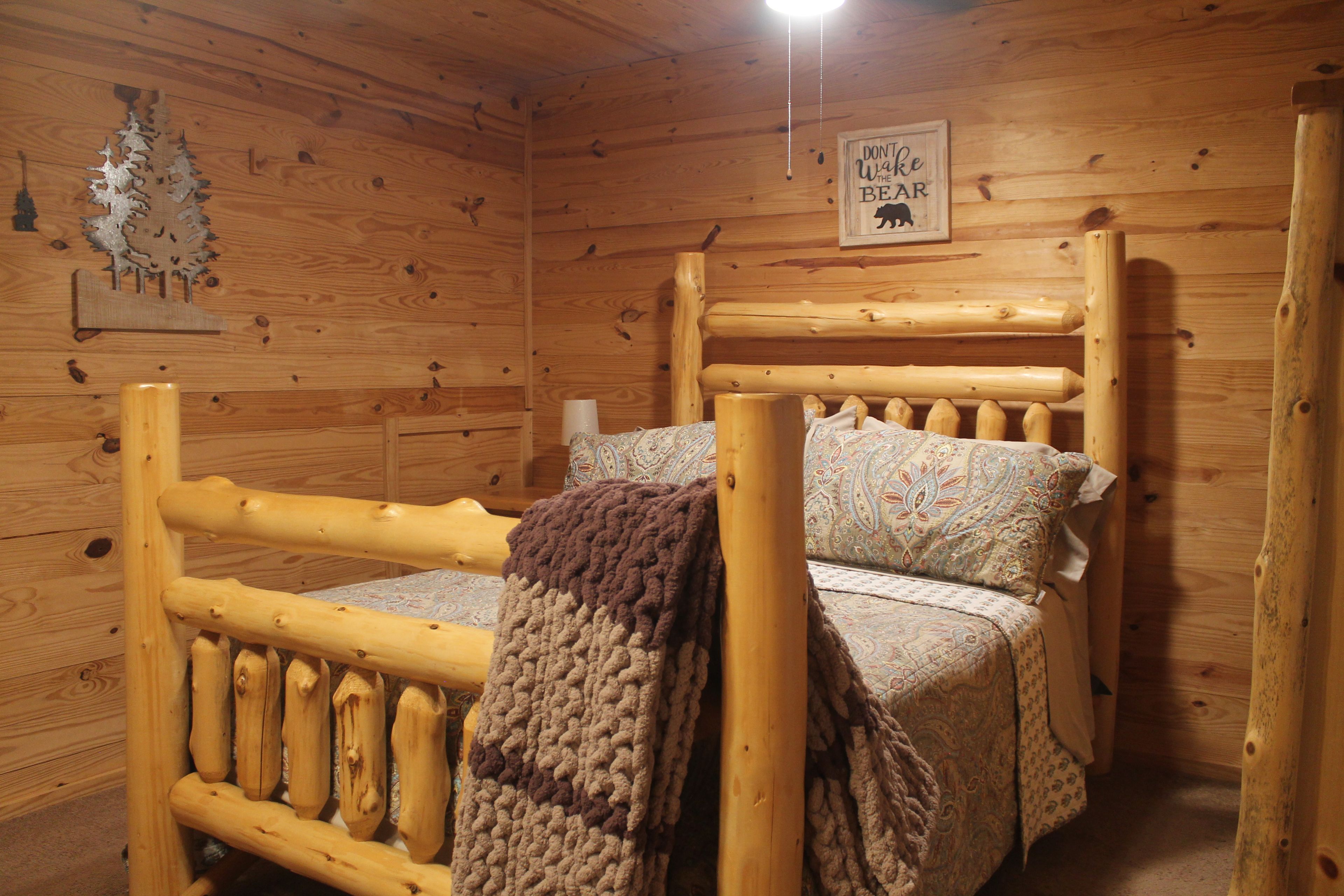 A wooden cabin interior with a bed, a wall sign, and a decorative tree cutout.