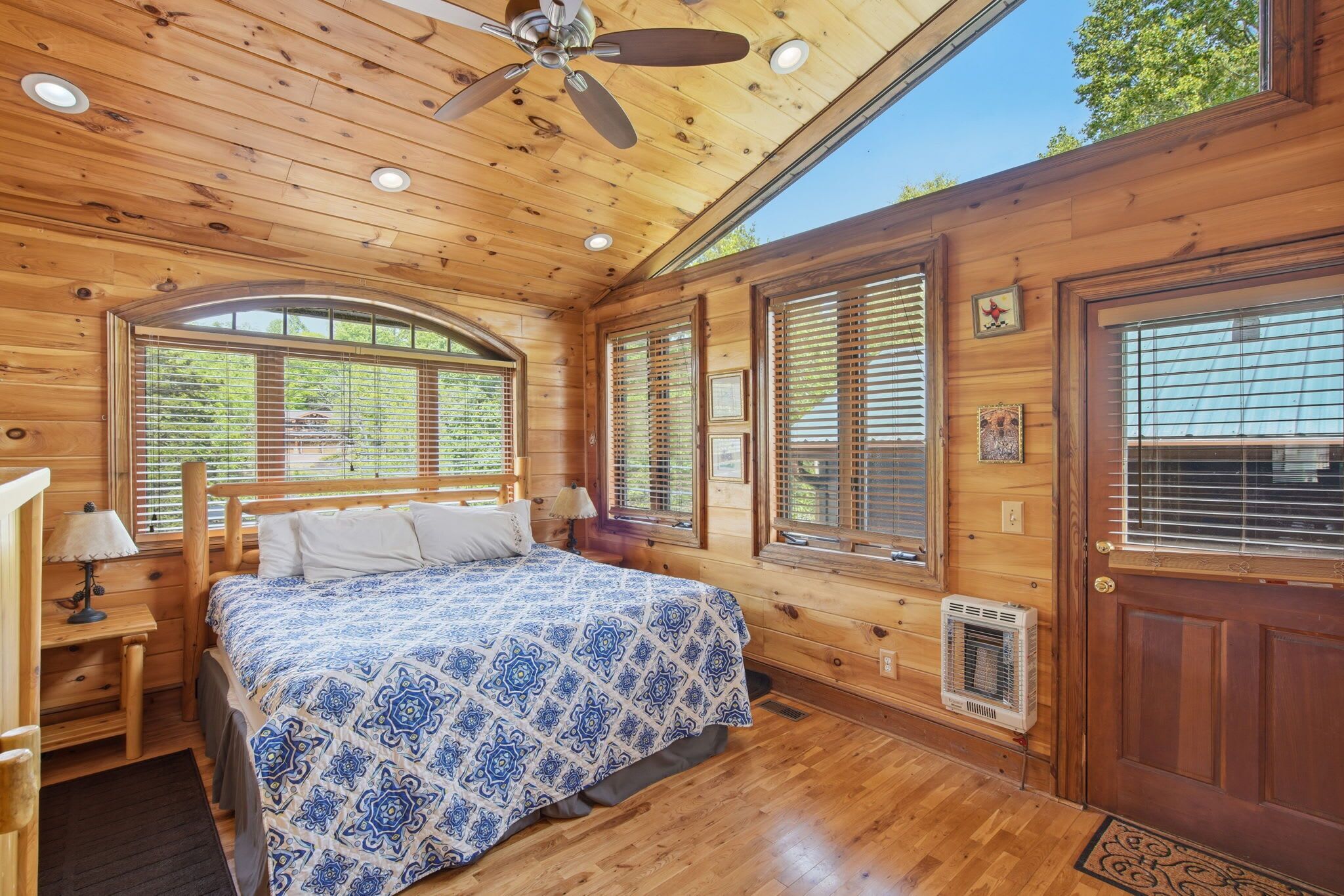 A wooden cabin bedroom with a bed, a ceiling fan, and large windows.