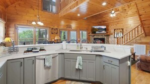 L’intérieur d’une cabane comprenant un grand îlot de cuisine, des armoires grises, une cheminée et un escalier en bois.