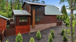 Une cabane en bois à deux étages, surmontée d’un toit en métal, entourée d’arbres et bordée d’une allée en gravier.