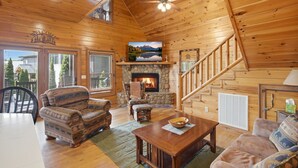 L’intérieur d’un chalet en bois, avec une cheminée, un coin repas et un escalier.