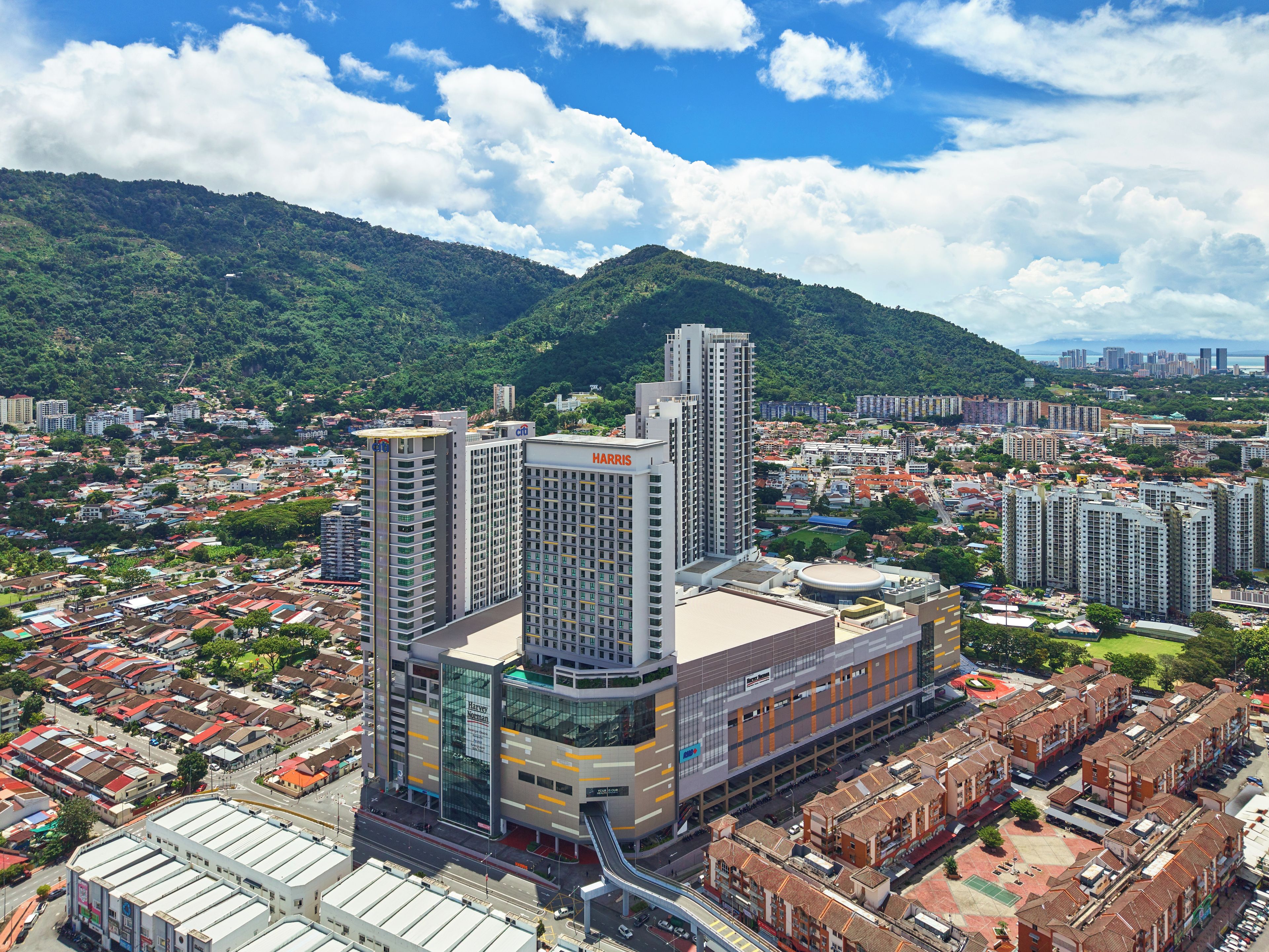 A high-rise building with multiple floors, surrounded by a densely populated urban area with various buildings and a mountainous backdrop.