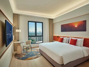 A hotel room with a large bed, a desk, a chair, a TV, and a city view.