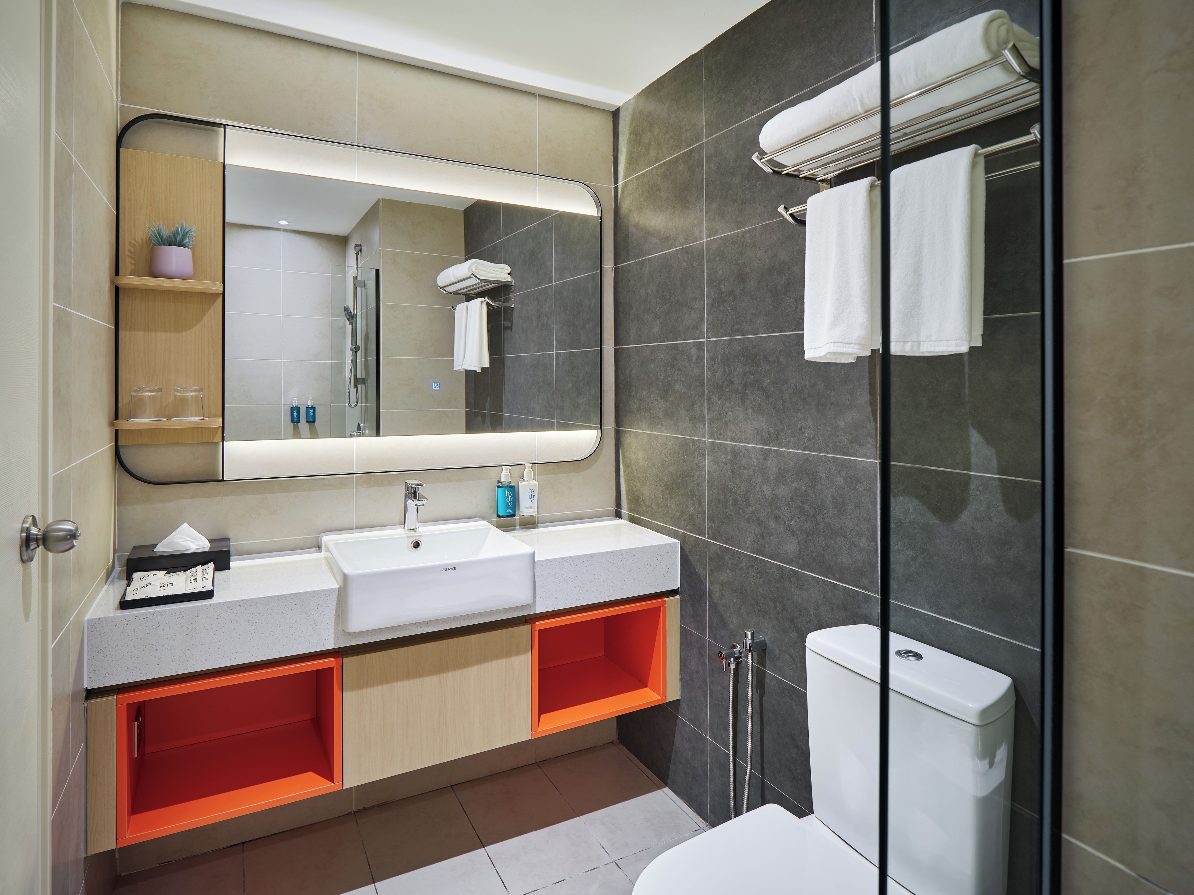 A modern bathroom with a large mirror, two sinks, a toilet, and a shower area.