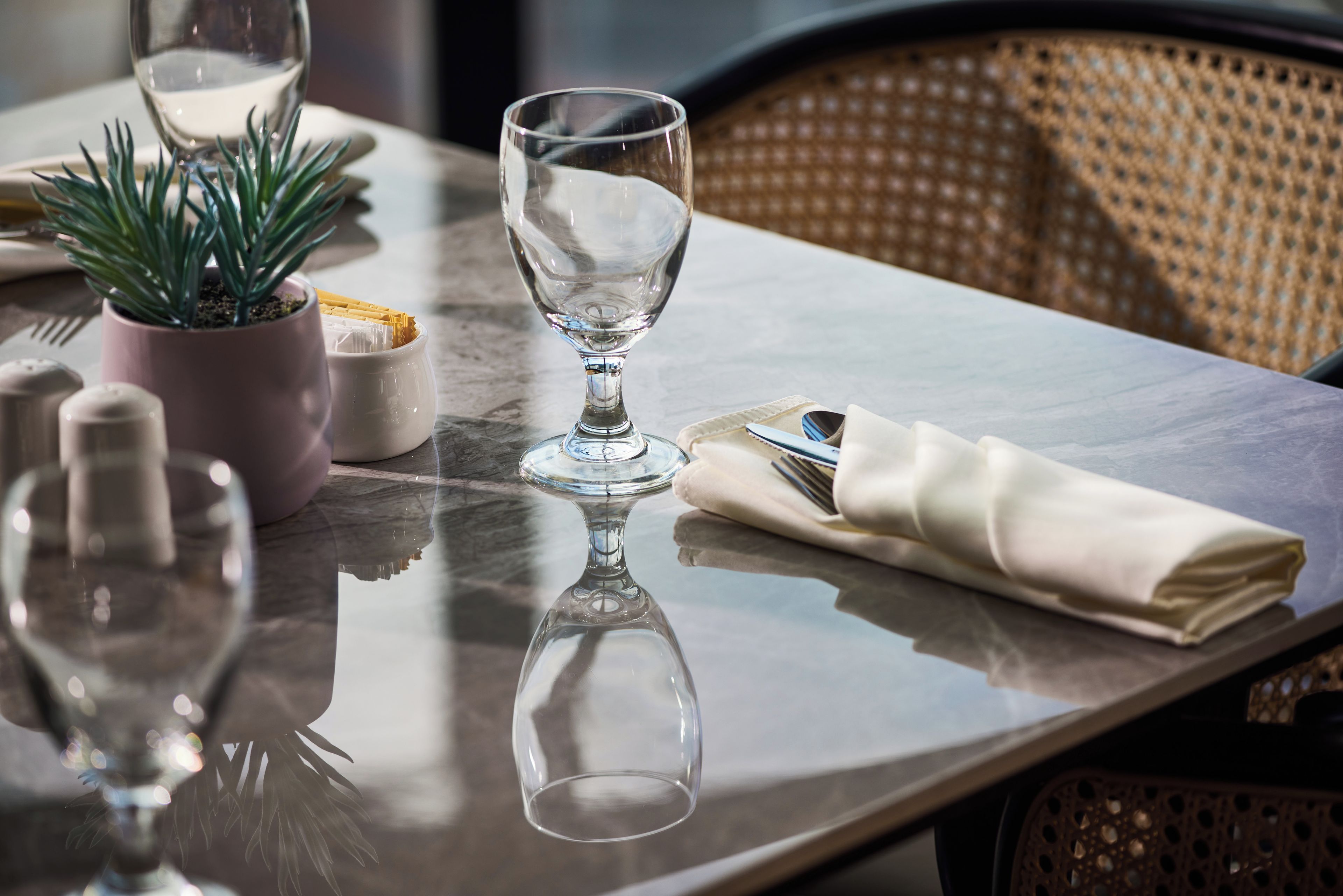A dining table with a clear glass, a potted plant, salt and pepper shakers, and a folded napkin with cutlery.