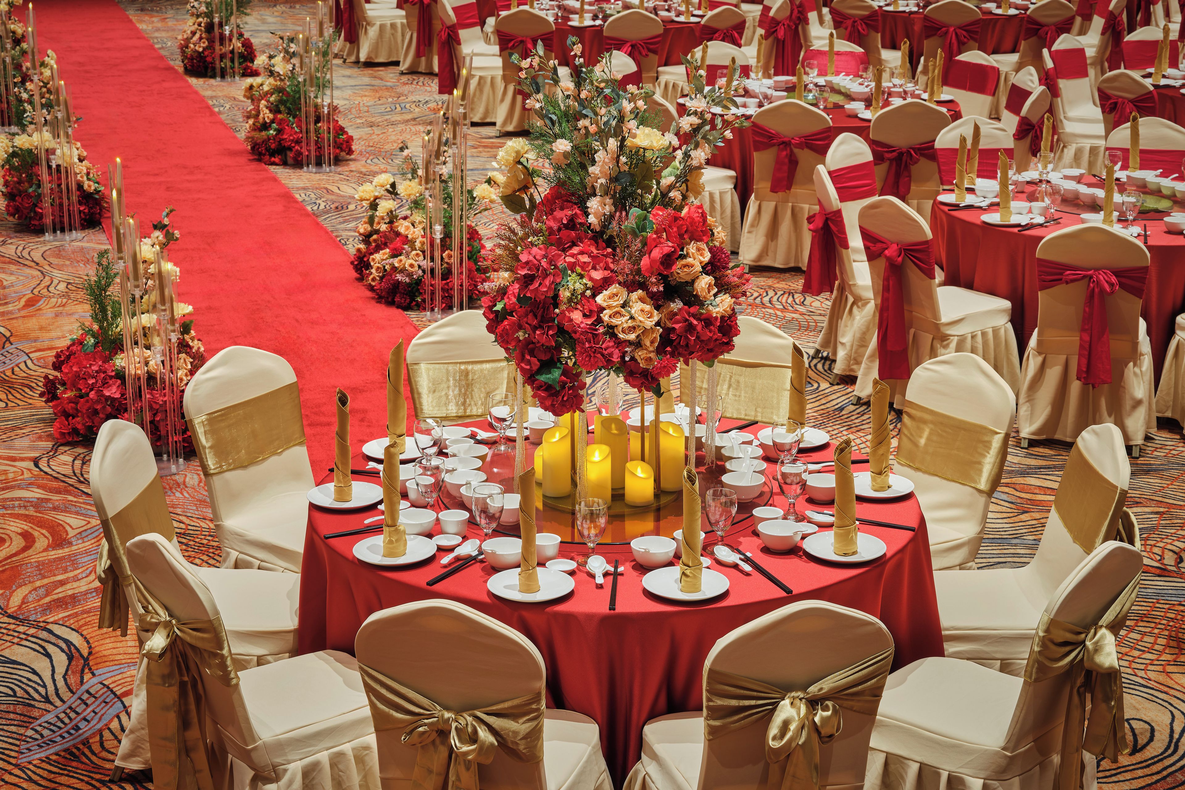 A banquet hall with round tables set for a formal event, featuring floral centerpieces and red tablecloths.