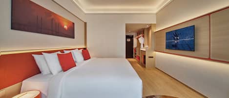 Una habitación de hotel con una cama grande, una mesita de noche, un televisor montado en la pared y un cuadro.
