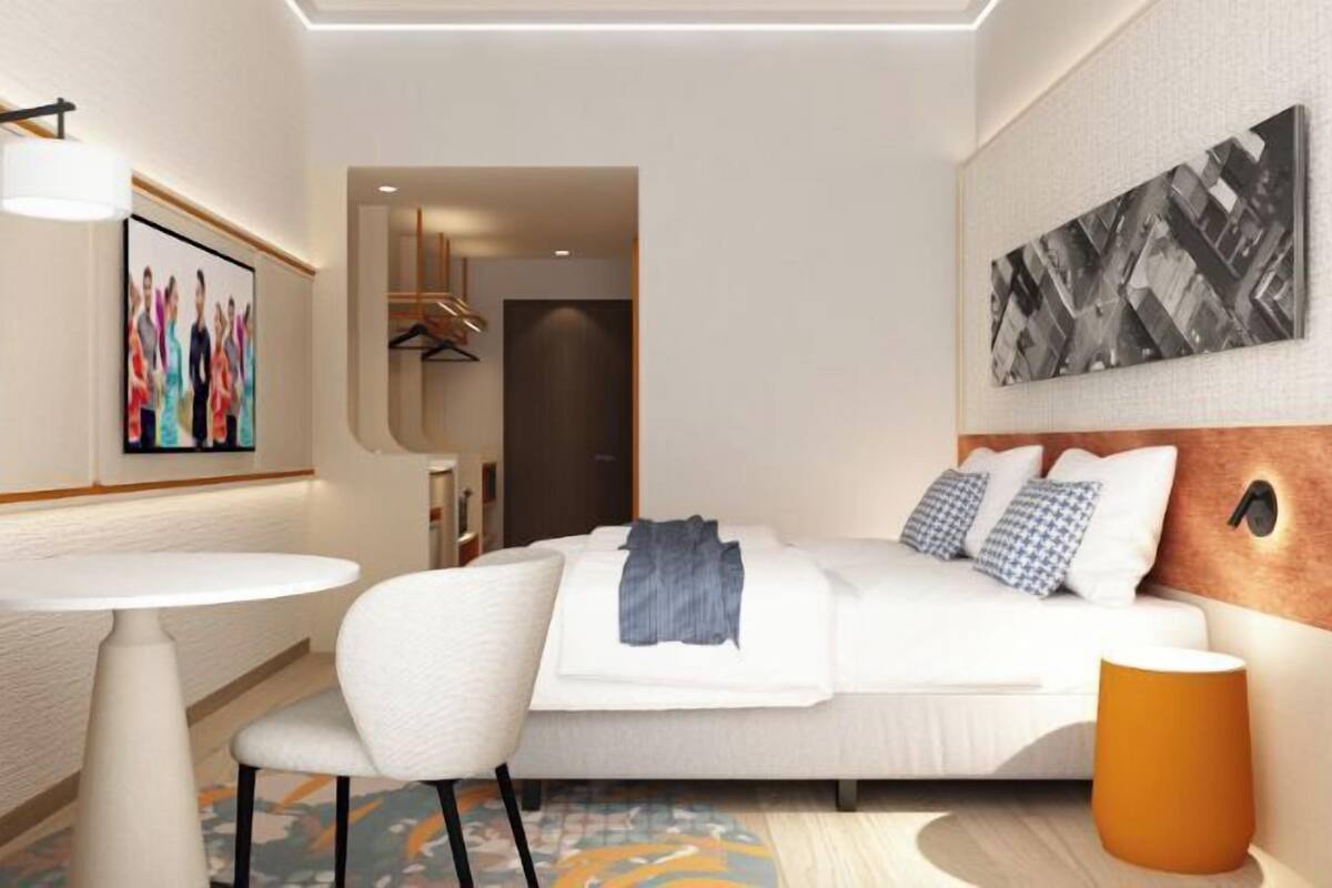 A hotel room with a bed, a round table, a chair, a lamp, and artwork on the walls.
