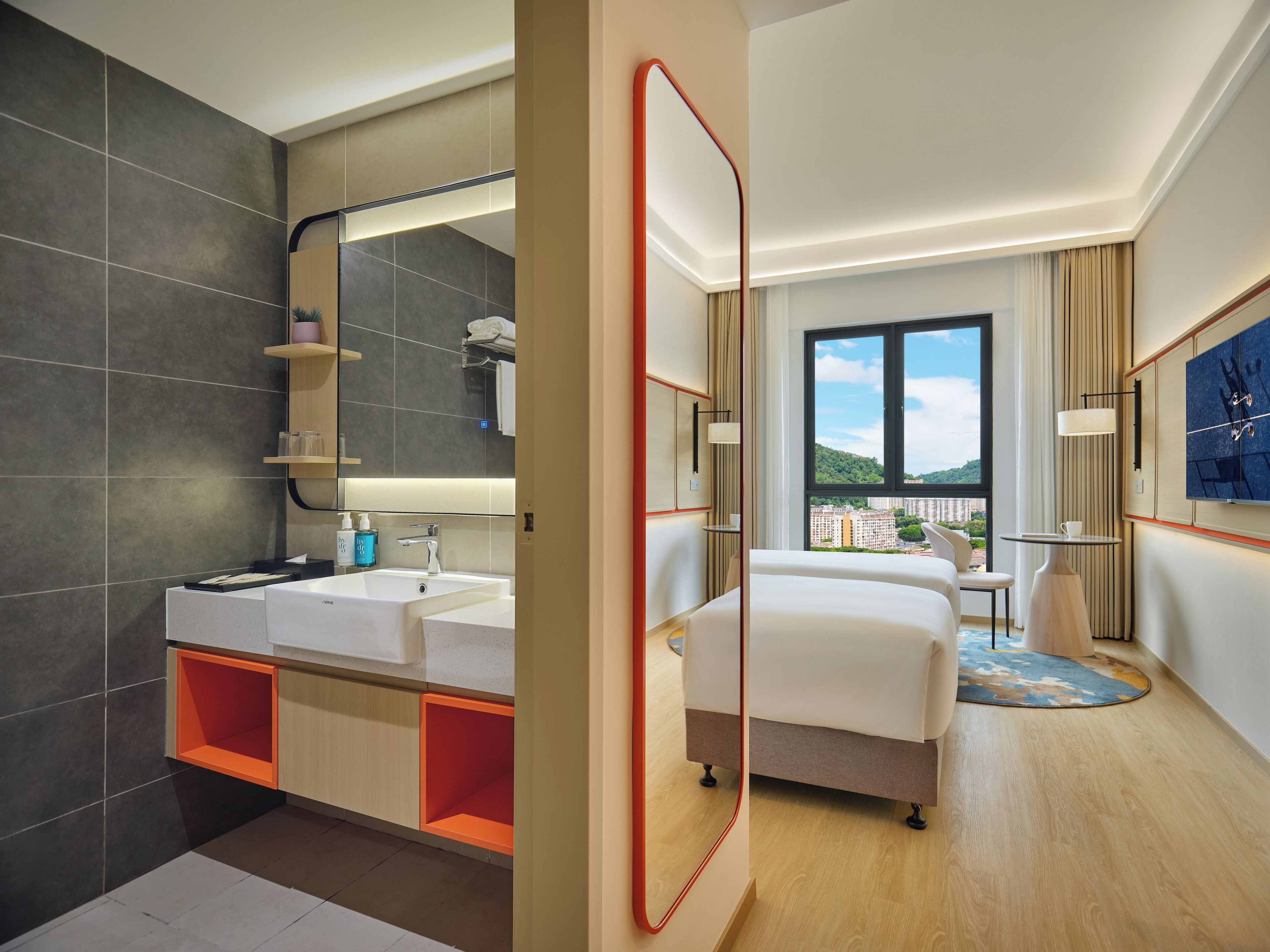 A modern hotel room with a large bed, a double sink, and a city view.