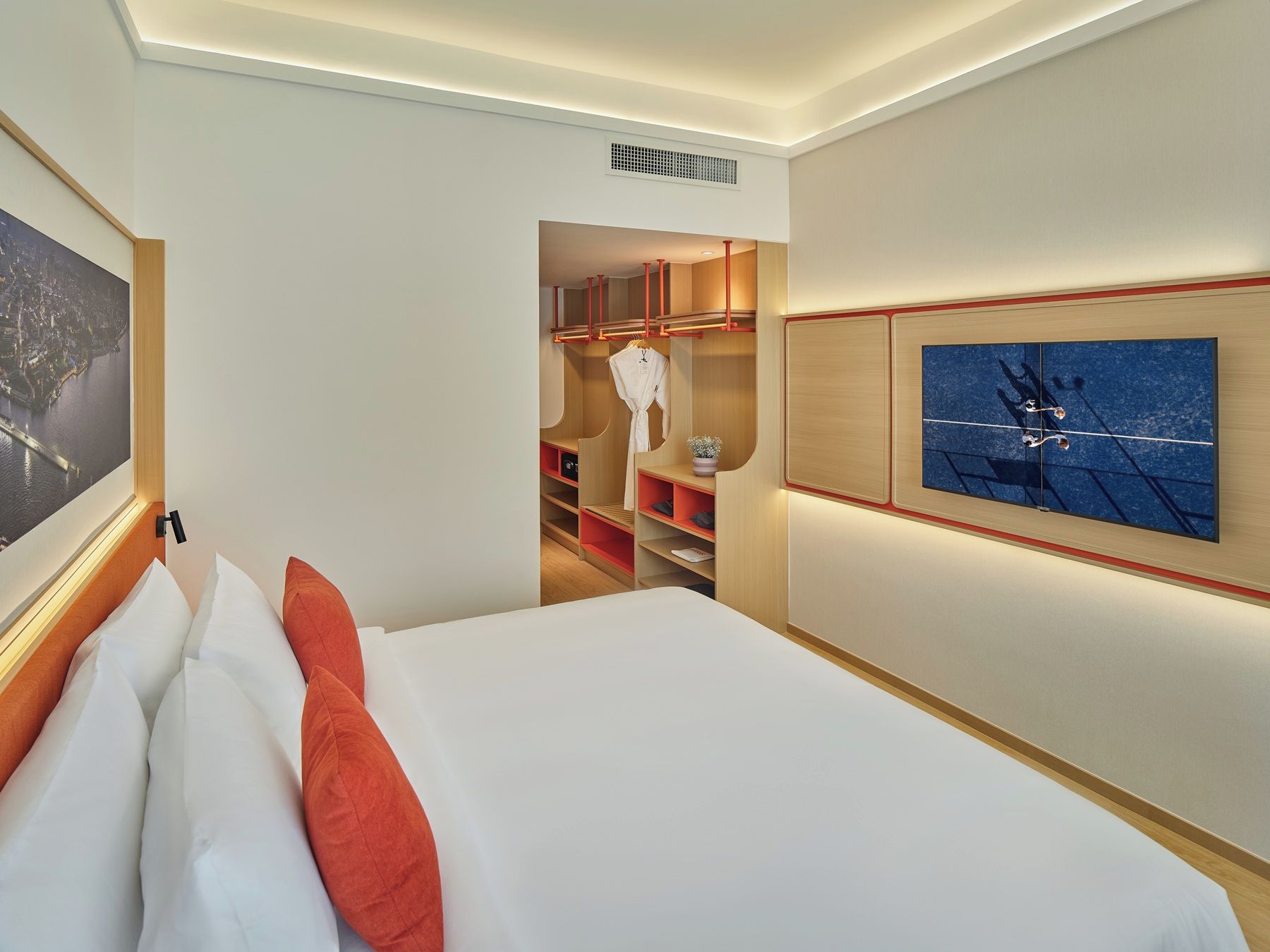 A hotel room with a bed, a nightstand, a wardrobe, a mirror, and a wall-mounted artwork.