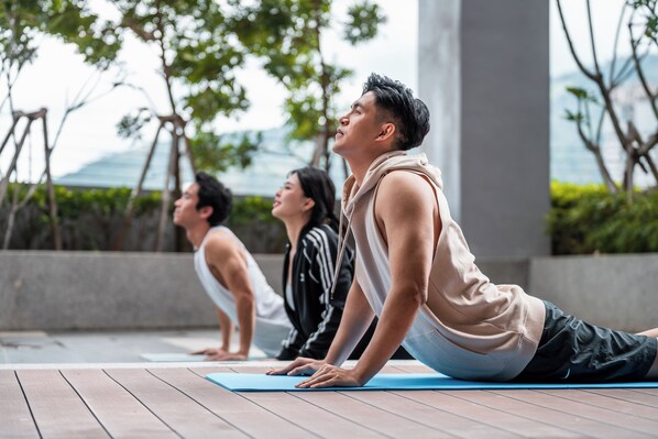 Three individuals performing yoga on a wooden deck with a view of trees and a building in the background.