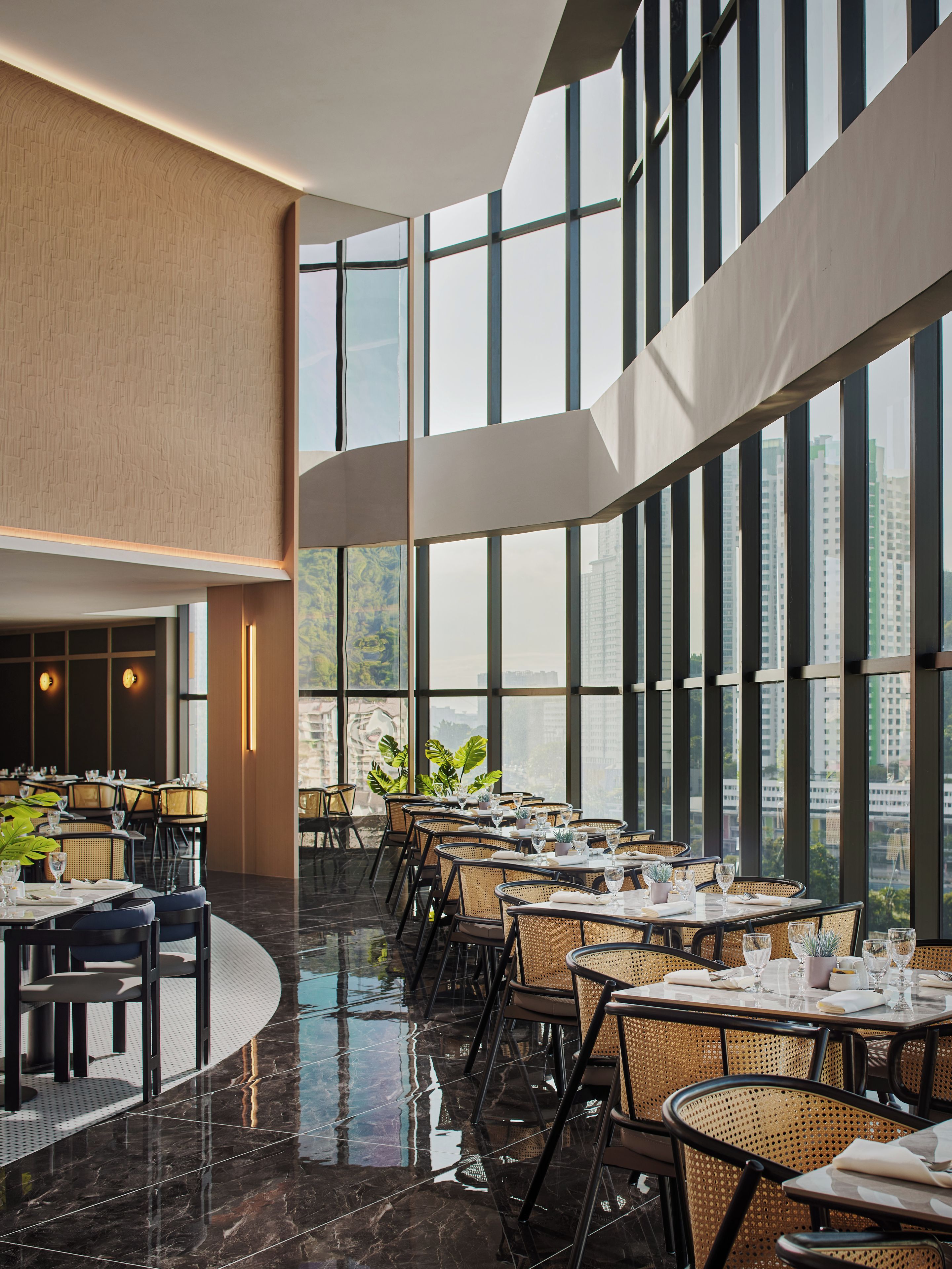 A modern restaurant with high ceilings and large windows, featuring a polished marble floor and a variety of seating arrangements.