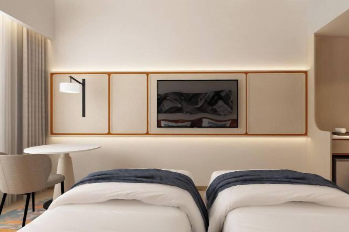 A modern hotel room with a bed, a desk, a chair, and a framed picture on the wall.