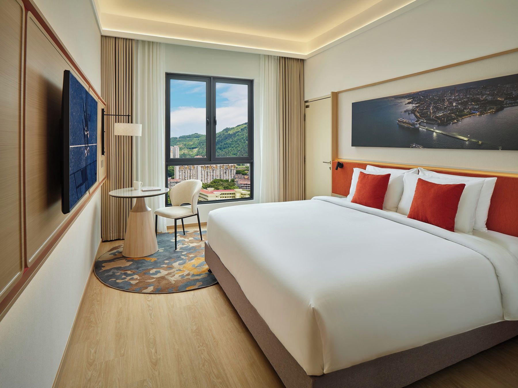 Ein Hotelzimmer mit Bett, Fernseher, Tisch mit Stuhl und einem Balkon mit Blick.