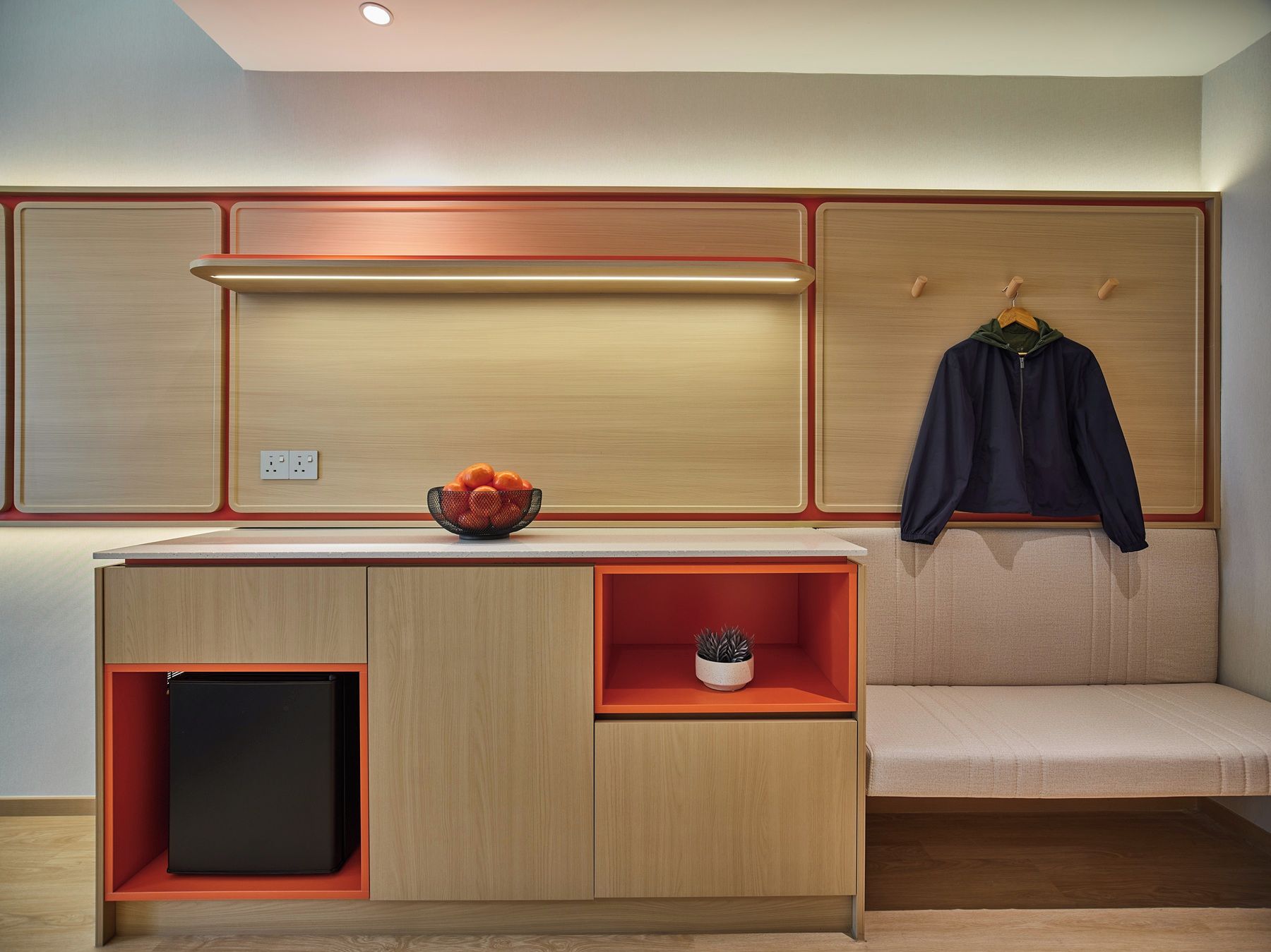 Una kitchenette moderna con horno integrado, un refrigerador pequeño y una zona de estar con un banco.