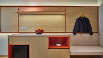Una kitchenette moderna con horno integrado, un refrigerador pequeño y una zona de estar con un banco.