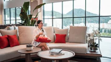 Eine Person sitzt auf einem Sofa und blickt durch große Fenster auf eine Stadtlandschaft.