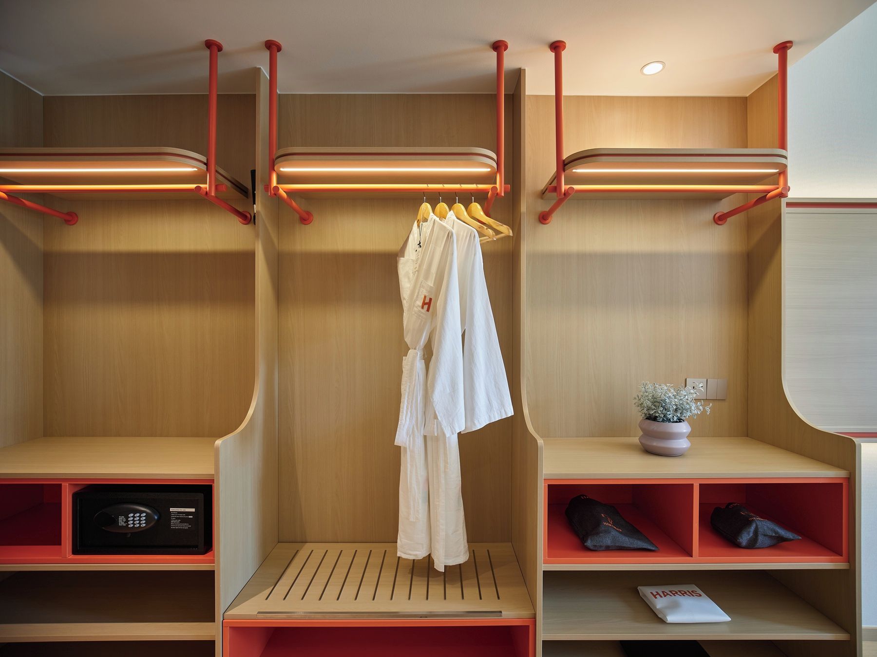 A modern walk-in closet with wooden shelving, red hanging rods, and a small seating area with a potted plant.