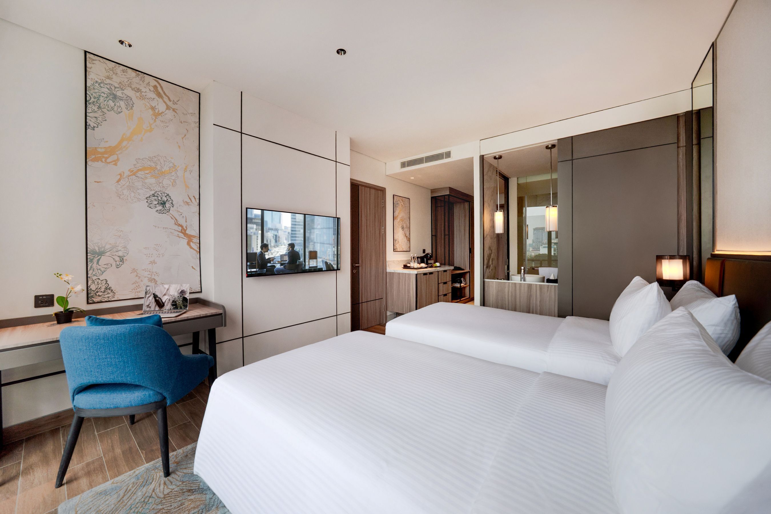 A hotel room with a large bed, a desk with a chair, a mirror, and a view of the city.