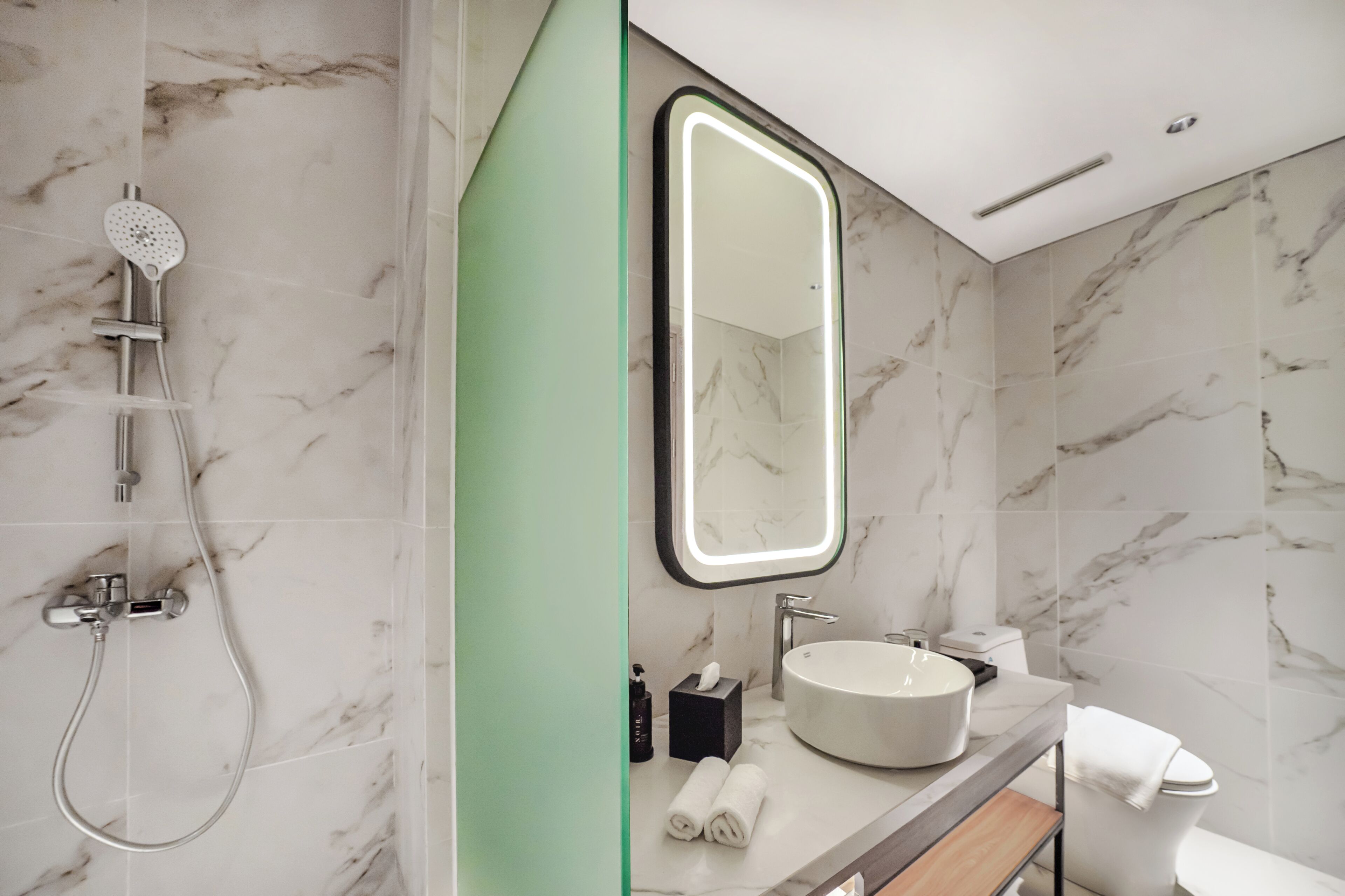Une salle de bain moderne avec une douche en marbre, un grand miroir, un lavabo et des toilettes.