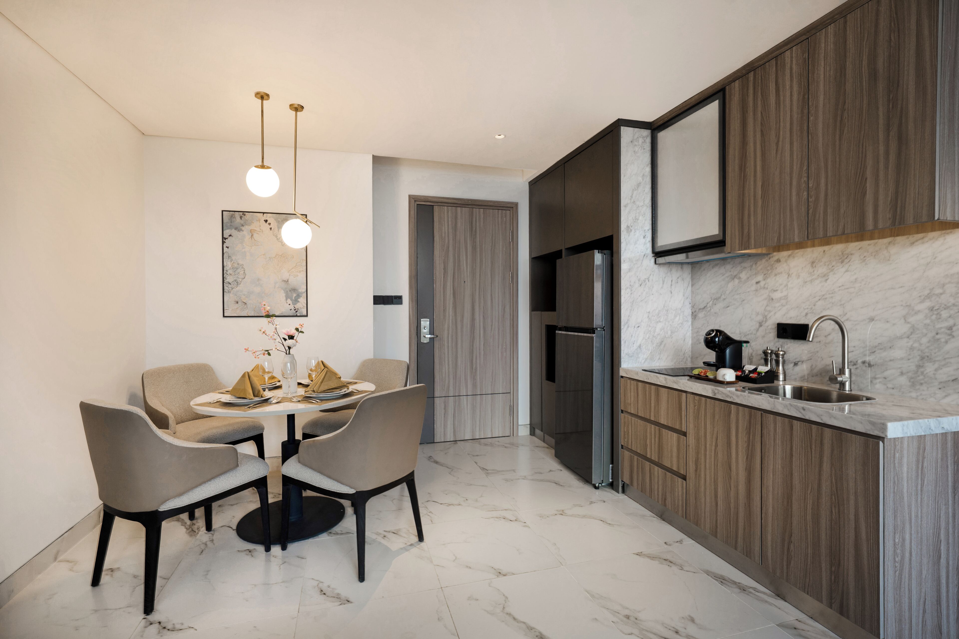 Cozinha moderna com bancada de mármore, armários de madeira embutidos, geladeira de aço inoxidável e área de jantar com mesa redonda e cadeiras.