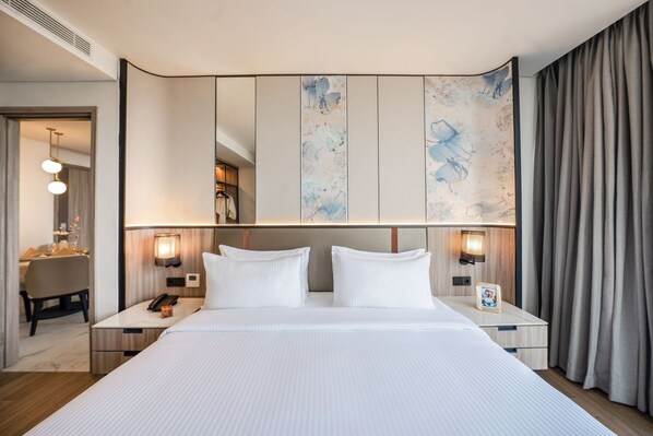 Une chambre d’hôtel avec un grand lit, deux tables de chevet, une petite table d’appoint, un bureau avec une chaise et un grand miroir au-dessus du lit.