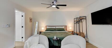 Un dormitorio con cama, ventilador de techo, lámparas de noche, televisor y una mesita.