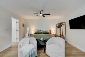 Ein Schlafzimmer mit einem Bett, einem Deckenventilator, Nachttischlampen, einem Fernseher und einem kleinen Tisch.