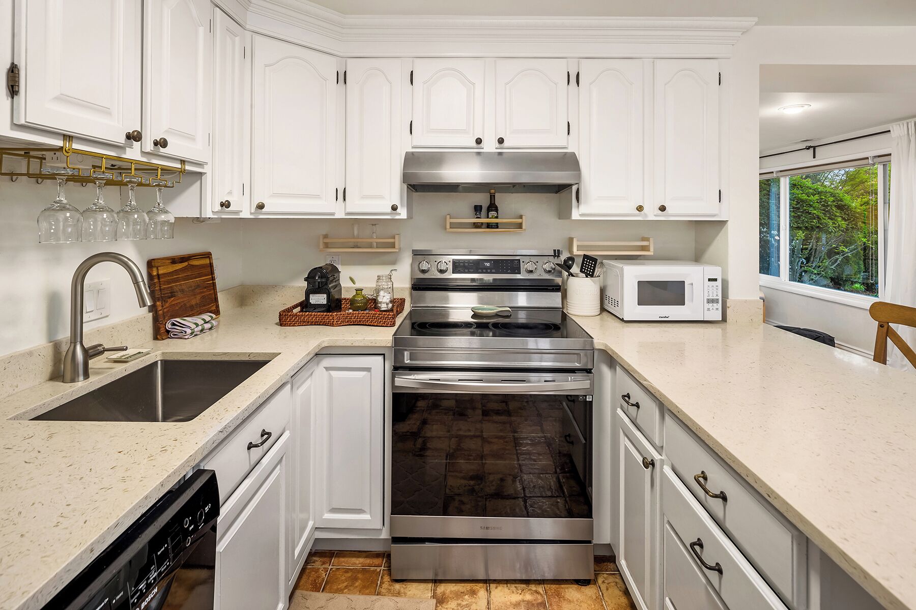 A modern kitchen with white cabinetry, stainless steel appliances, and a window providing a view of greenery.