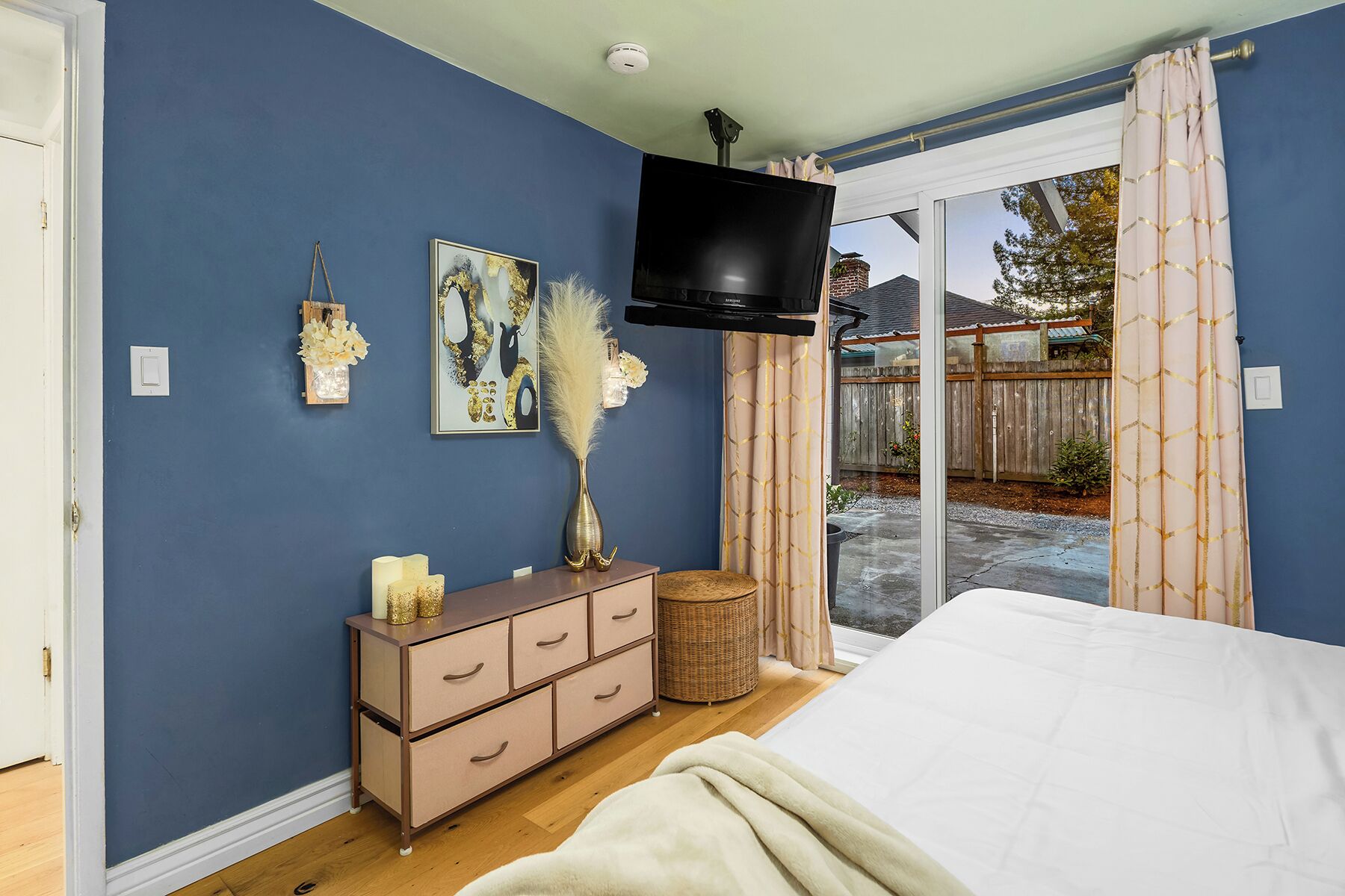 A bedroom with a bed, a dresser, a TV, and a sliding glass door to a patio.