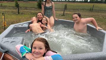 Un bain à remous doté d’une structure en bois et d’une structure en métal, entouré d’un champ verdoyant.
