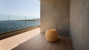 Un balcón con vistas al mar y a barcos, un taburete tejido y una decoración interior moderna.