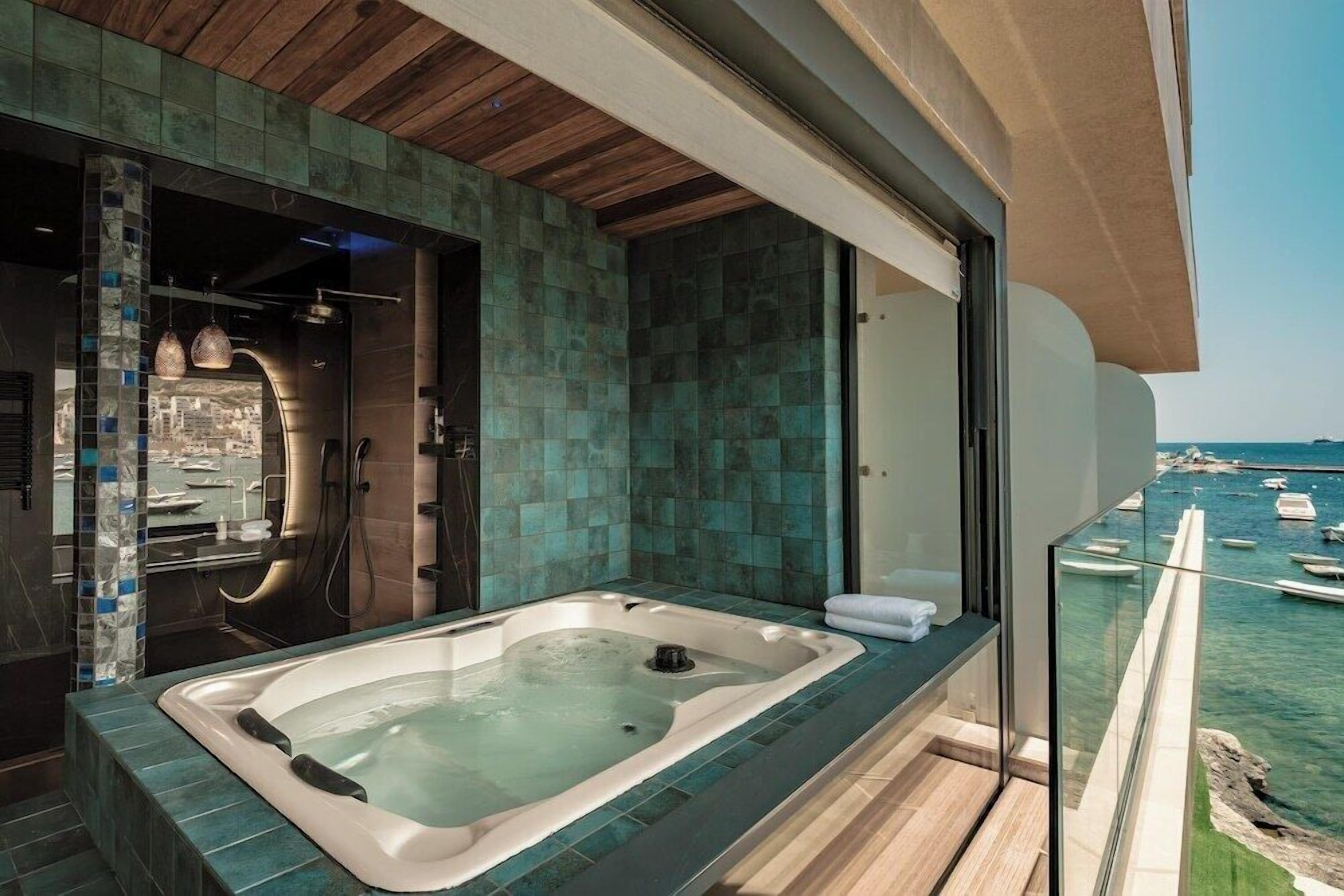 A modern bathroom with a large bathtub, a shower area, and a glass-enclosed balcony overlooking a marina.