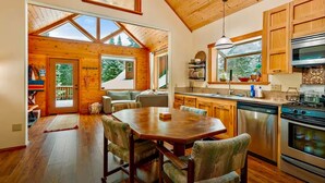 A spacious kitchen with wooden cabinets, a dining area with a large table, and a view of the outdoors through skylights. - Woodlake Retreats Cozy Cabin + decks and firepit (Ashland)
