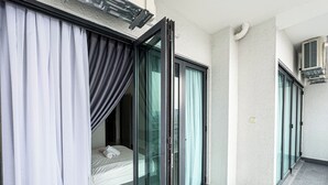 Ein modernes Hotelzimmer mit einer Schiebetür zu einem Balkon, einem Bett mit weißem Kopfteil und einem kleinen Fenster.