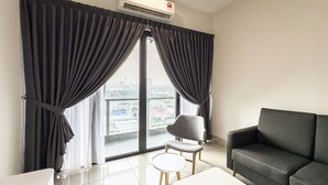 Ein modernes Wohnzimmer mit einer Couch, einem kleinen runden Tisch und einem Sessel. Es gibt ein großes Fenster mit Vorhängen, eine Klimaanlage und einen Blick auf eine Skyline.