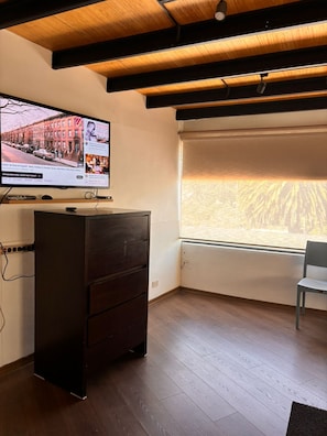 A room with a wooden ceiling, a TV on a stand, a window with a view, and a chair. - Apartment near Carolina Park (Quito)