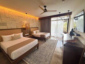 A hotel room with a large bed, a smaller bed, a desk, a ceiling fan, and a view of the outdoors.