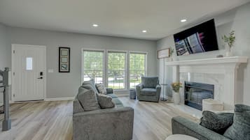 A living room with a fireplace, a large window, and a grey sofa.