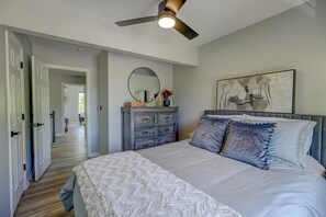A bedroom with a bed, dresser, ceiling fan, and artwork on the wall.