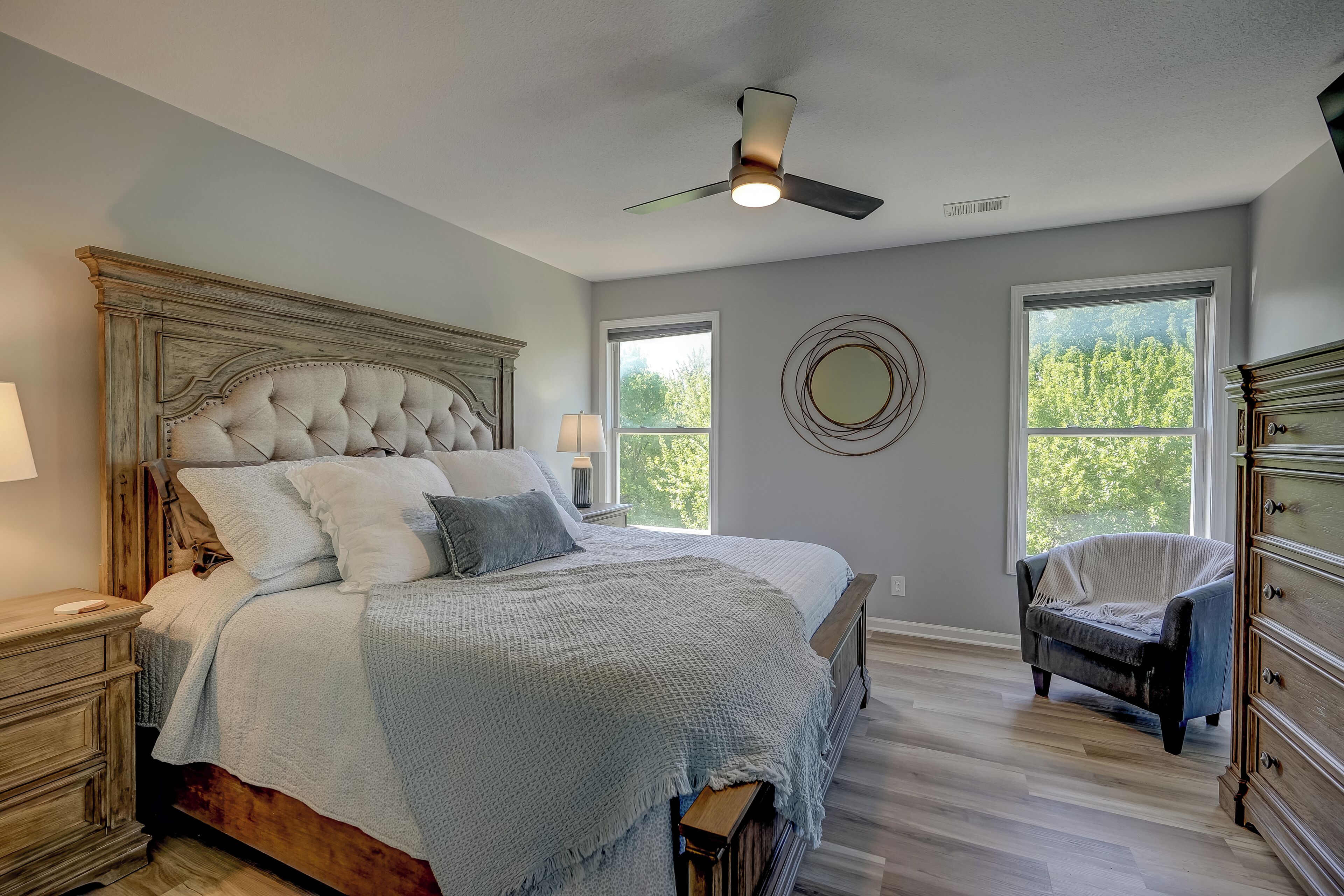 A bedroom with a large bed, a ceiling fan, a dresser, and two windows.