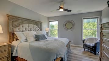 A bedroom with a large bed, a ceiling fan, a dresser, and two windows.