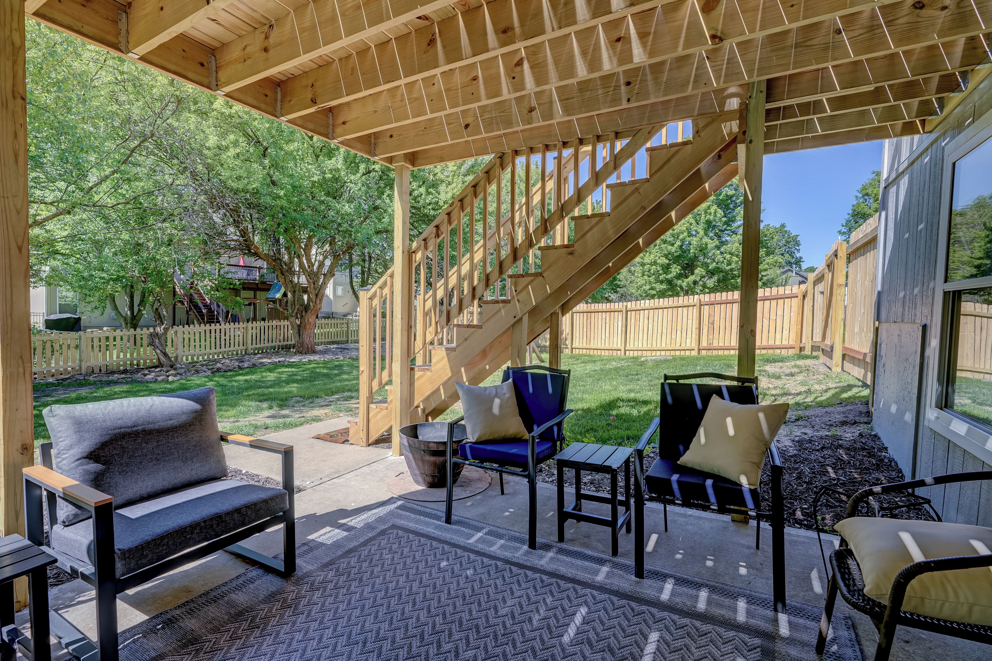 A covered patio area with outdoor furniture, a wooden staircase, and a view of the backyard.