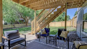 A covered patio area with outdoor furniture, a wooden staircase, and a view of the backyard.