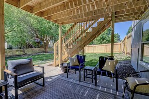 Un patio couvert aménagé avec du mobilier d’extérieur, un escalier en bois et une vue sur le jardin arrière.